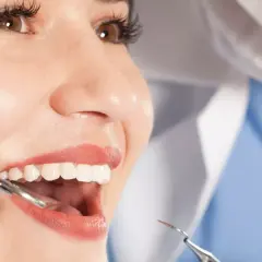 Uśmiechnięta pacjentka podczas badania stomatologicznego. Dentysta bada zęby, by zapobiec abrazji.