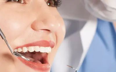 Uśmiechnięta pacjentka podczas badania stomatologicznego. Dentysta bada zęby, by zapobiec abrazji.
