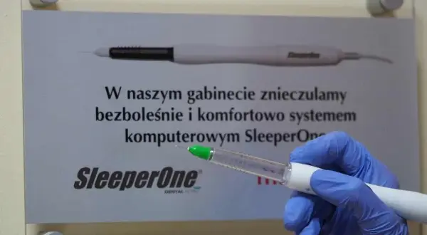 Ręka w niebieskiej rękawiczce trzymająca komputerowy system znieczulający SleeperOne.