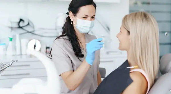 Dentystka bada uśmiech pacjentki. Może to być kontrola po uderzeniu, gdy ruszający się ząb mleczny u dziecka wymaga uwagi.