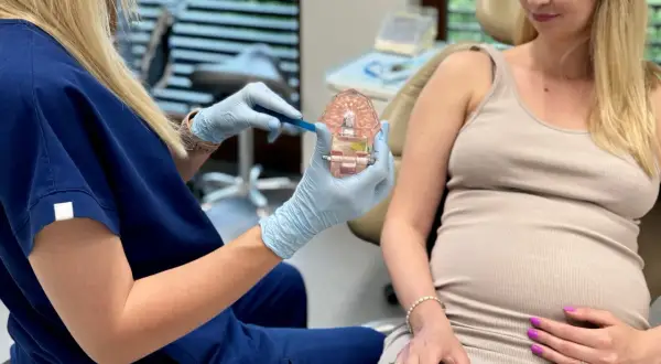 Dentystka pokazuje ciężarnej pacjentce prawidłową higienizację zębów w ciąży na modelu szczęki.