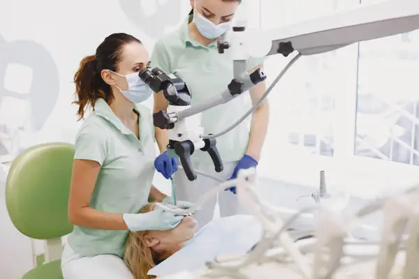 Dentystka z asystentką przy mikroskopie stomatologicznym, przygotowujące się do zabiegu, być może wyrywania ósemki.