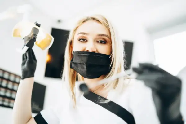 Uśmiechnięta dentystka w masce przygotowuje się do lakierowania zębów, trzymając lampę i narzędzia.