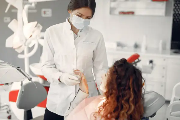 Dentystka w masce podaje wodę pacjentce. Bezpieczne leczenie kanałowe w ciąży jest możliwe.