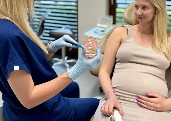 Dentystka pokazuje ciężarnej pacjentce prawidłową higienizację zębów w ciąży na modelu szczęki.